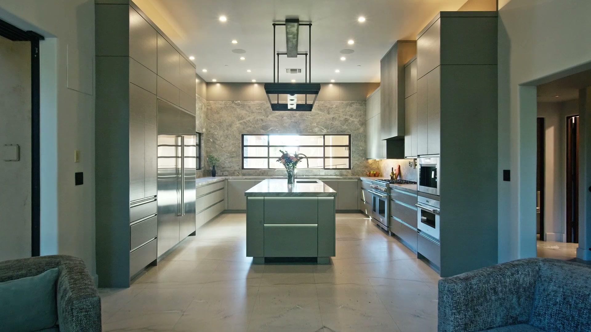 A cinematic film frame of the kitchen, the stone island beneath the suspended steel hood